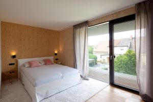 Schlafzimmer mit großer Terrassentüre und Ausblick über die Nachbarschaft (Paschinger Architekten)